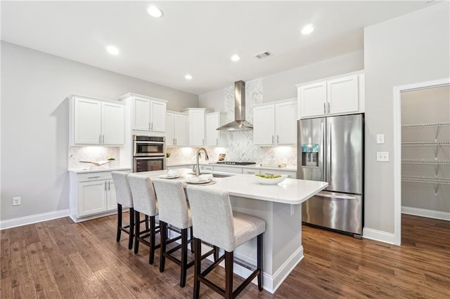 kitchen with wall chimney range hood, a center island with sink, a kitchen bar, stainless steel appliances, and a sink