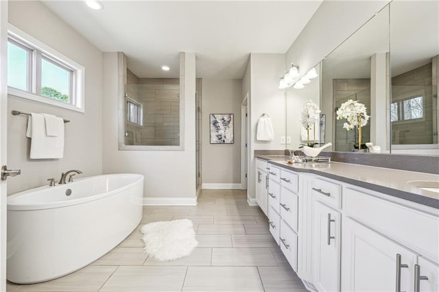 full bathroom featuring recessed lighting, a shower stall, double vanity, baseboards, and a freestanding bath