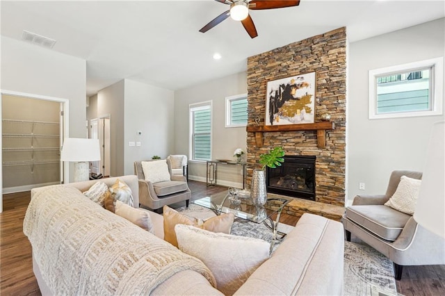 living room featuring visible vents, wood finished floors, a stone fireplace, baseboards, and ceiling fan