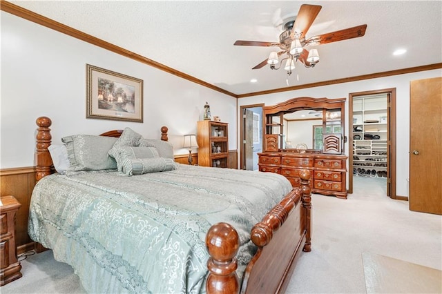 carpeted bedroom featuring a closet, wood walls, a walk in closet, ornamental molding, and ceiling fan