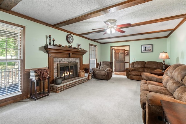 carpeted living room featuring a fireplace, a textured ceiling, beam ceiling, ceiling fan, and ornamental molding