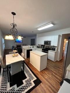 kitchen with white cabinetry, a kitchen island, stainless steel appliances, hardwood / wood-style flooring, and decorative light fixtures