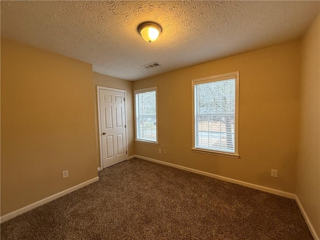 unfurnished room featuring baseboards, visible vents, dark colored carpet, and a textured ceiling