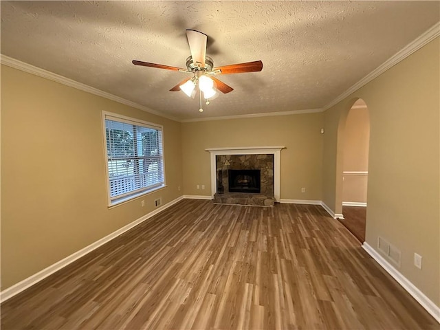 unfurnished living room with arched walkways, crown molding, ceiling fan, wood finished floors, and baseboards