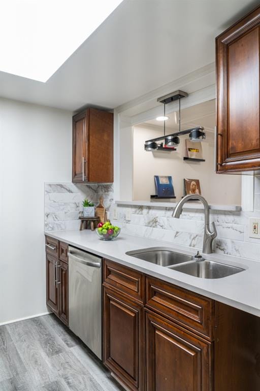 kitchen with a skylight, dishwasher, sink, backsplash, and light hardwood / wood-style floors