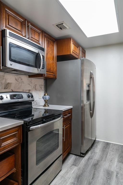 kitchen with appliances with stainless steel finishes, light hardwood / wood-style floors, and decorative backsplash