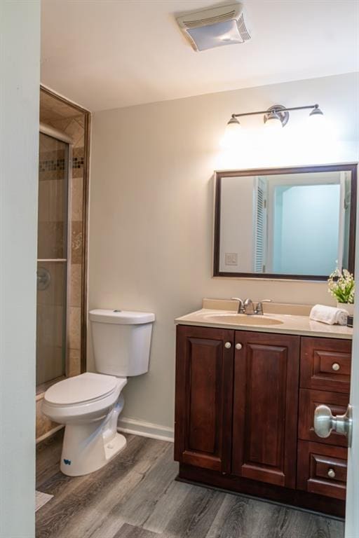 bathroom featuring hardwood / wood-style flooring, vanity, a shower with shower door, and toilet