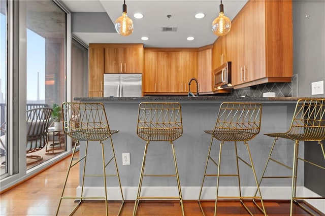 1080 Peachtree St NE Unit 2108, Atlanta, GA 30309 - kitchen featuring appliances with stainless steel finishes, tasteful backsplash, brown cabinetry, hanging light fixtures, and a kitchen bar