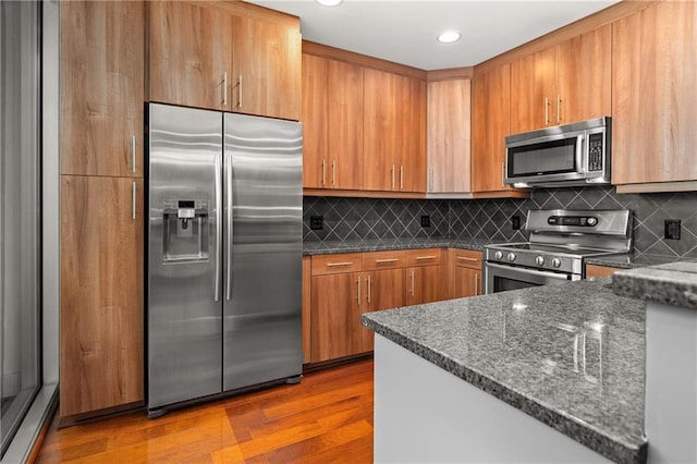 1080 Peachtree St NE Unit 2108, Atlanta, GA 30309 - kitchen with stainless steel appliances, dark stone counters, backsplash, wood finished floors, and brown cabinetry