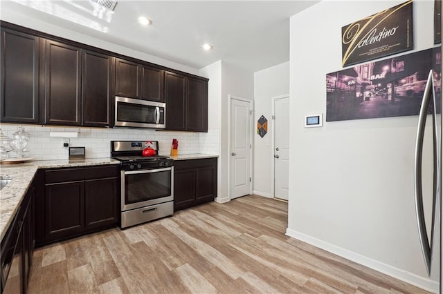 kitchen with appliances with stainless steel finishes, tasteful backsplash, dark brown cabinetry, light stone countertops, and light hardwood / wood-style flooring