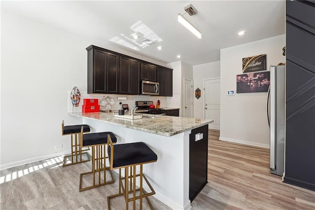 kitchen featuring tasteful backsplash, kitchen peninsula, stainless steel appliances, light stone countertops, and light hardwood / wood-style flooring