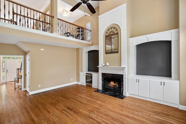 unfurnished living room featuring beverage cooler, baseboards, a towering ceiling, wood finished floors, and a high end fireplace