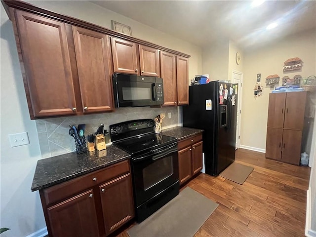 kitchen featuring baseboards, dark stone counters, decorative backsplash, light wood-style flooring, and black appliances