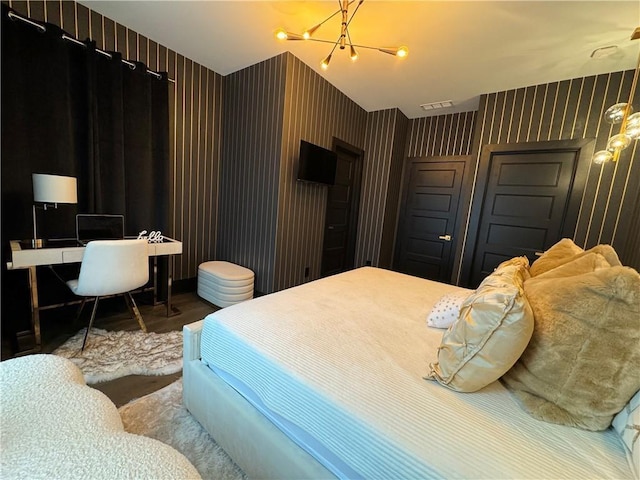 bedroom with wood finished floors, visible vents, an inviting chandelier, and wallpapered walls