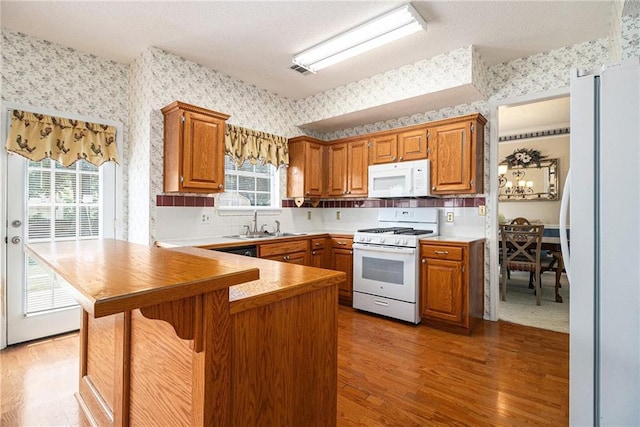 1900 Green Oak Cir, Lawrenceville, GA 30043 - kitchen featuring white appliances, wallpapered walls, light wood-type flooring, a peninsula, and a kitchen bar