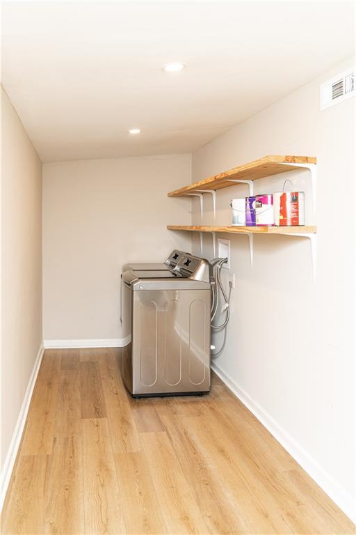 clothes washing area featuring water heater, washer / clothes dryer, and light hardwood / wood-style floors