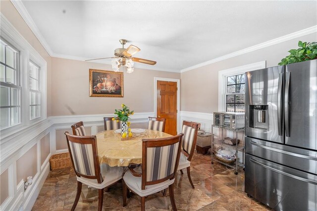 4983 Arcado Rd SW, Lilburn, GA 30047 - dining space with marble finish floor, crown molding, a decorative wall, a ceiling fan, and wainscoting