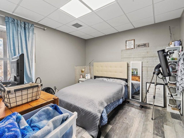 bedroom with a paneled ceiling, visible vents, and wood finished floors