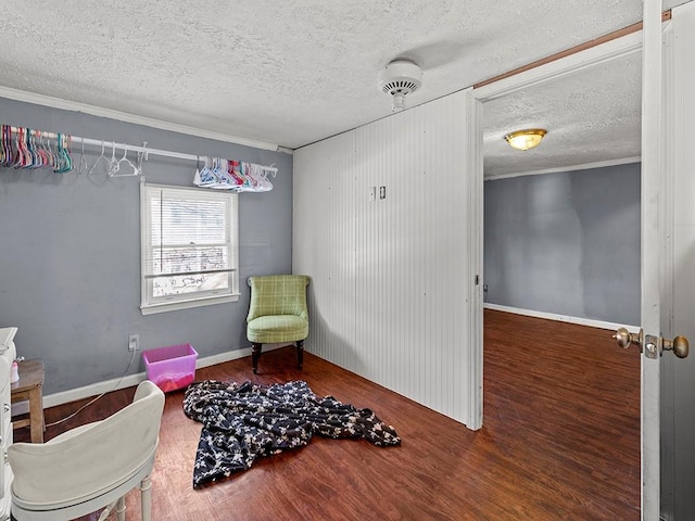 living area featuring a textured ceiling, ornamental molding, wood finished floors, and baseboards