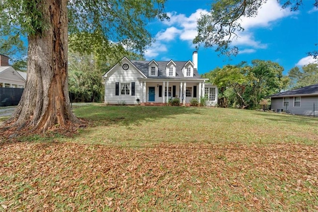 new england style home with a front yard, covered porch, and a chimney