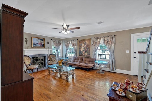 living area with visible vents, ceiling fan, stairway, wood finished floors, and a brick fireplace