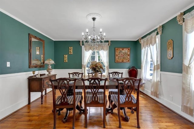 dining area featuring ornamental molding, wainscoting, a notable chandelier, and wood finished floors