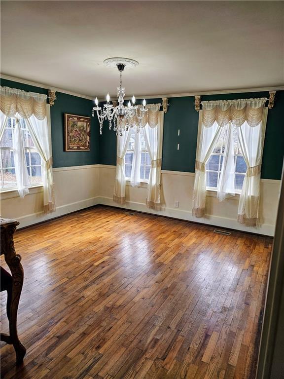 unfurnished dining area featuring visible vents, wainscoting, hardwood / wood-style flooring, and an inviting chandelier