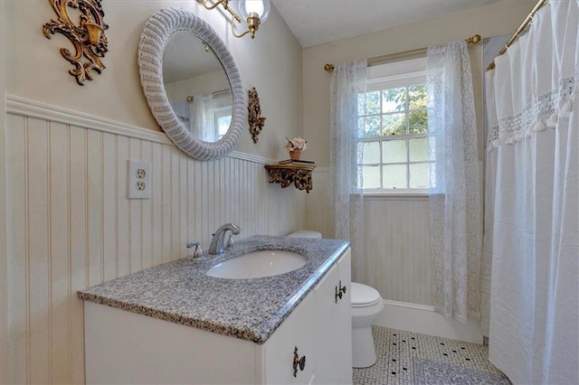 bathroom with toilet, a wainscoted wall, a shower with curtain, tile patterned floors, and vanity