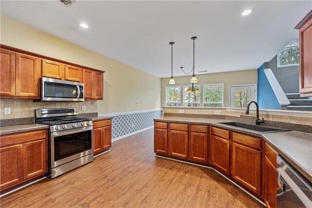 kitchen with sink, backsplash, light hardwood / wood-style floors, decorative light fixtures, and appliances with stainless steel finishes