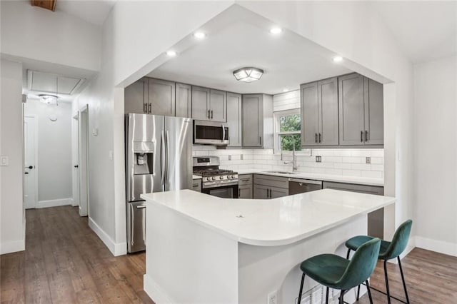 kitchen featuring dark wood-style floors, gray cabinets, a sink, decorative backsplash, and stainless steel appliances