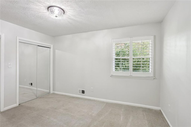 unfurnished bedroom featuring visible vents, a textured ceiling, a closet, and carpet flooring