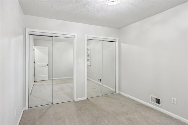 unfurnished bedroom featuring visible vents, multiple closets, a textured ceiling, carpet, and baseboards