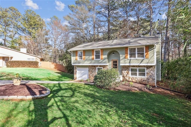 bi-level home featuring stone siding, fence, a front yard, a garage, and a chimney