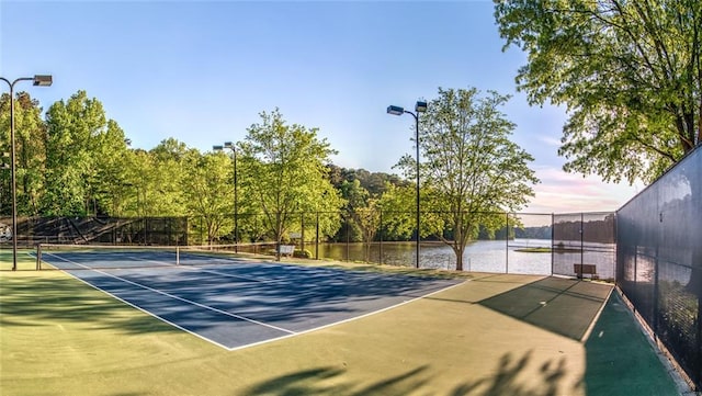 view of tennis court featuring fence and a water view