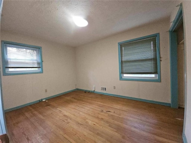 spare room with a textured ceiling, baseboards, wood finished floors, and visible vents