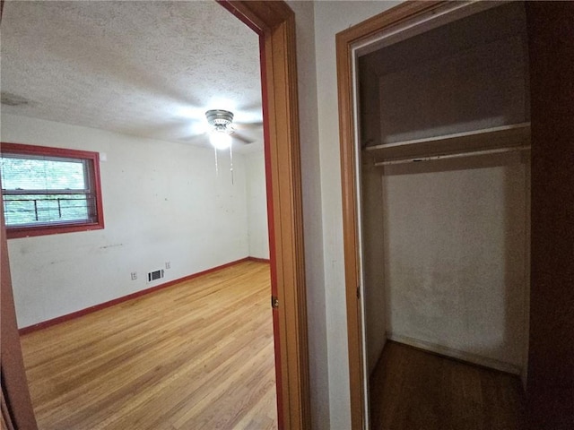 unfurnished bedroom featuring a textured ceiling, a ceiling fan, baseboards, wood finished floors, and visible vents