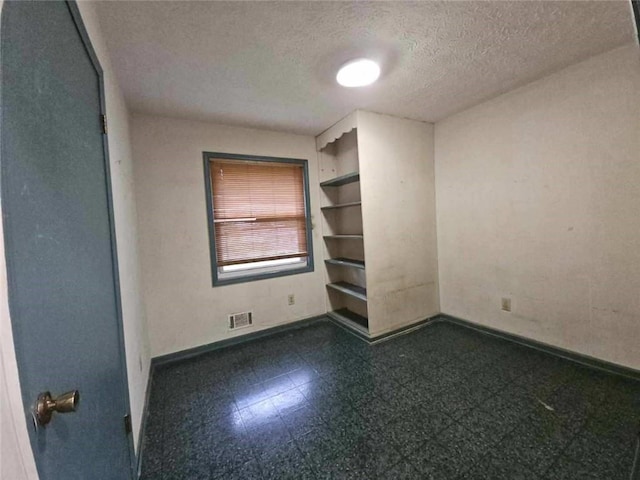 unfurnished room featuring a textured ceiling, visible vents, baseboards, and dark floors