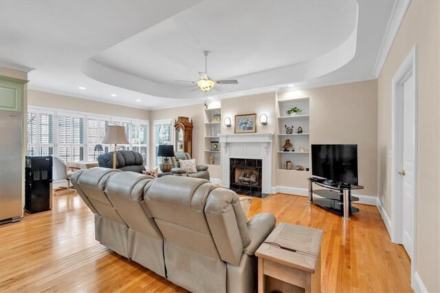 living room featuring a tray ceiling, baseboards, a tiled fireplace, and light wood finished floors