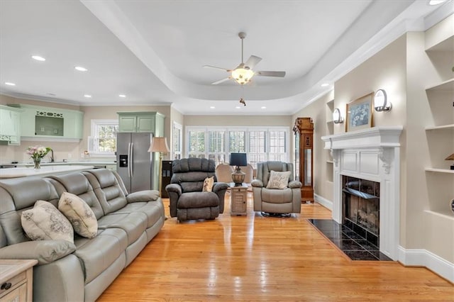 living room featuring baseboards, recessed lighting, a high end fireplace, light wood-style floors, and a raised ceiling