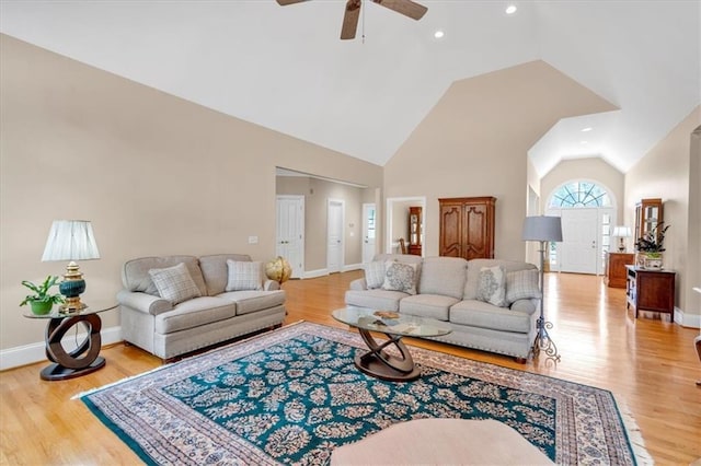 living room featuring ceiling fan, high vaulted ceiling, light wood-type flooring, and baseboards