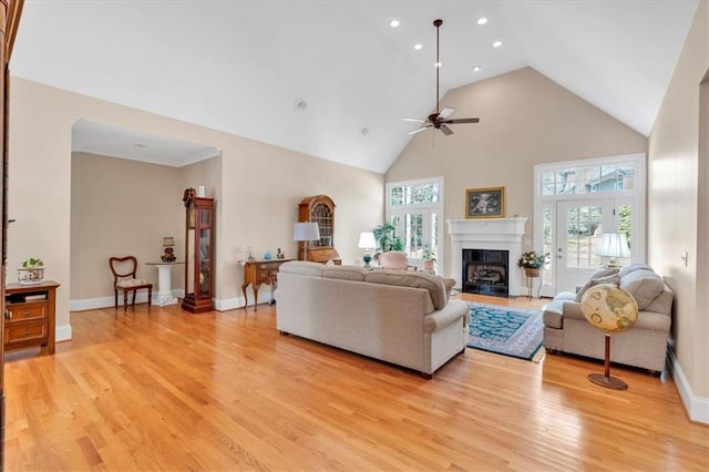 living room with baseboards, light wood finished floors, high vaulted ceiling, a fireplace, and ceiling fan