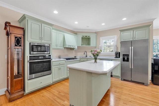 kitchen featuring light wood finished floors, a sink, light countertops, custom range hood, and appliances with stainless steel finishes