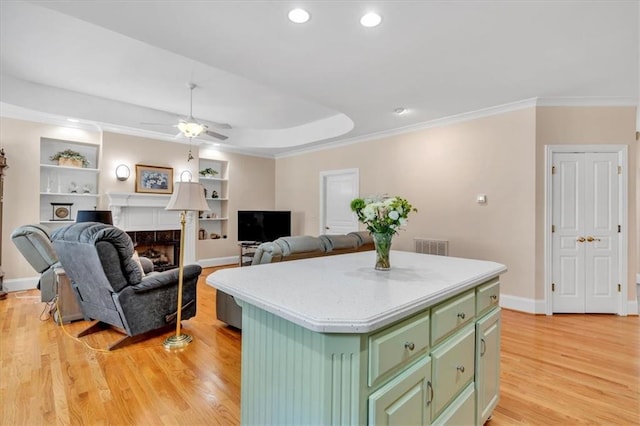 kitchen featuring a kitchen island, light wood-type flooring, ornamental molding, a fireplace, and green cabinetry