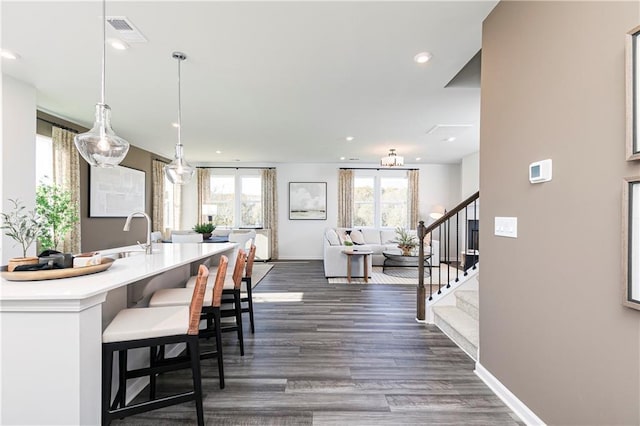 kitchen featuring a sink, dark wood-type flooring, light countertops, baseboards, and a kitchen bar