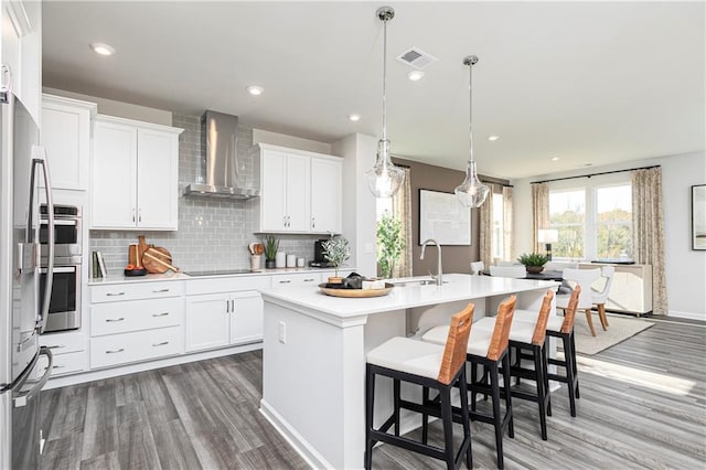 kitchen with wall chimney exhaust hood, a sink, wood finished floors, light countertops, and an island with sink