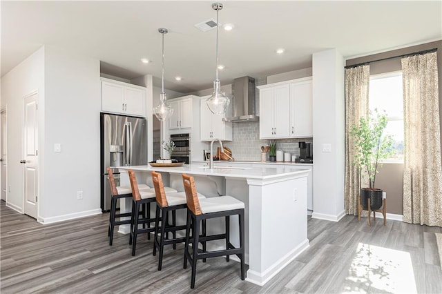 kitchen featuring wall chimney exhaust hood, stainless steel appliances, light wood finished floors, light countertops, and recessed lighting