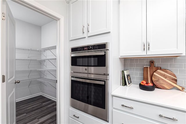 kitchen featuring stainless steel double oven, white cabinetry, decorative backsplash, and light countertops