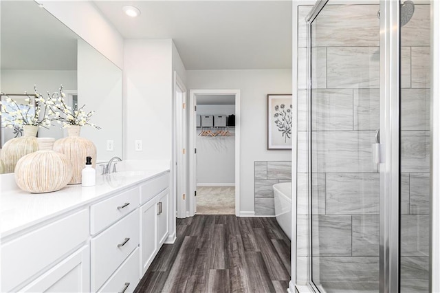 full bathroom with wood finished floors, vanity, a shower stall, a spacious closet, and a soaking tub