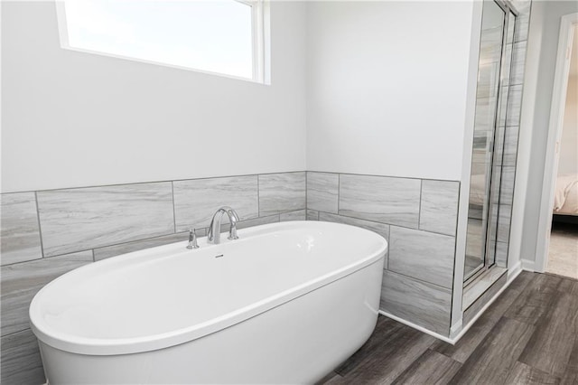 ensuite bathroom featuring wood finished floors and a soaking tub