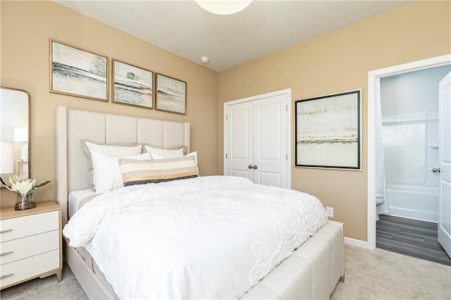 bedroom with a closet, light colored carpet, connected bathroom, and baseboards